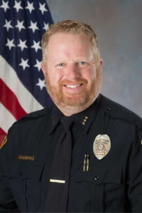 "Assistant Chief Christopher Dennison in TPD uniform next to American flag"